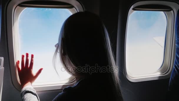 Девочке 6 лет, она смотрит в окно самолета. Вид сзади, в рамке видны иллюминаторы — стоковое видео