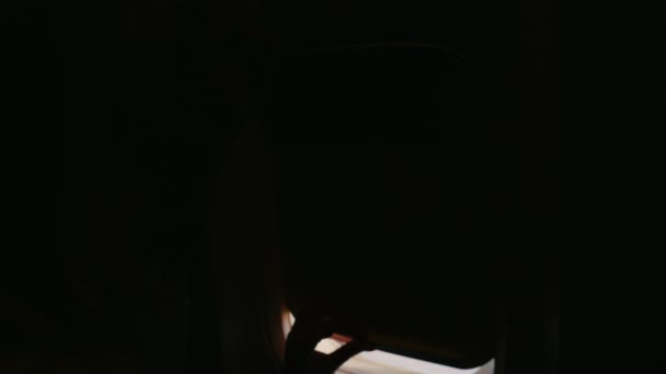 Een jonge vrouw wordt een vliegtuig geopend en kijkt uit het raam. De donkere frame brandt met de opening van het gordijn — Stockvideo