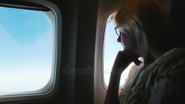 Eine nachdenkliche Frau fliegt im Flugzeug, schaut aus dem Fenster. Seitenansicht, Silhouette — Stockvideo