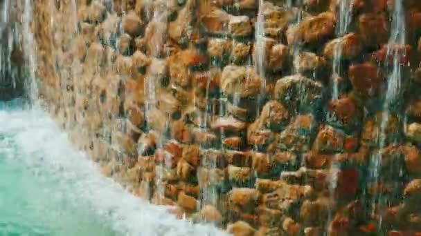 Наклонный кадр: Декоративный водопад. Пейзаж дизайн тропического курорта. Вода стекает по каменной стене — стоковое видео