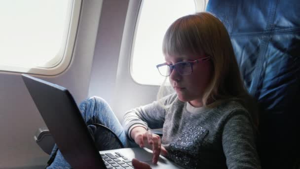 Una joven mujer de negocios en gafas vuela en un avión, utiliza una computadora portátil. Rubia chica caucásica 6 años — Vídeos de Stock