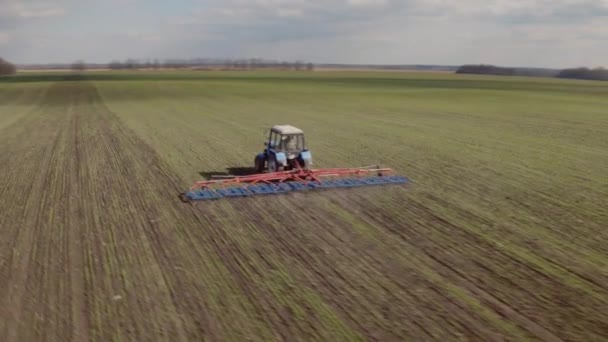 Трактор обрабатывает землю в поле ранней весной. Камера летает вокруг — стоковое видео
