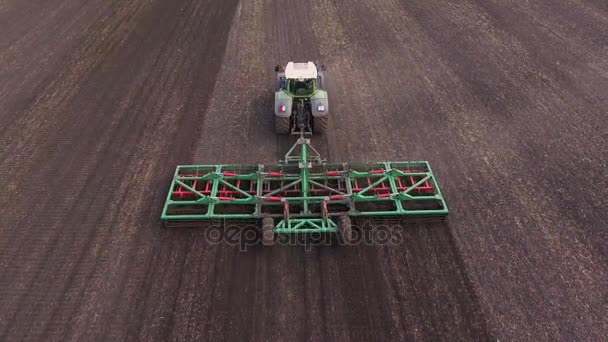 Plan incliné : Le tracteur dessine un dispositif agricole pour herser la terre. Travail de printemps sur le terrain, vidéo aérienne 