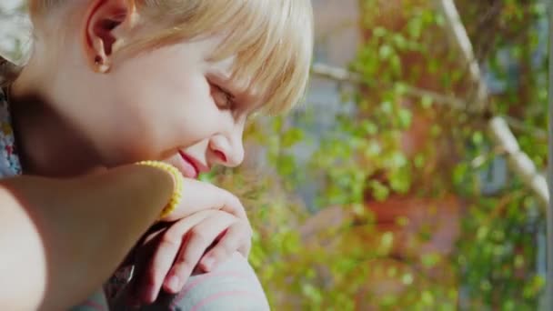 Portrait d'une fille blonde réfléchie de 6 ans. Il regarde par la fenêtre, un jour de printemps clair, devant la fenêtre un bouleau frais se balançant dans le vent. Concept de rêves de bébé 