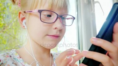 Güzel sarışın kız telefonu kullanımı 6 yıllık. Onu kulaklıktan gülüyor, güneşin olumlu duygular. Pencere cama oturur