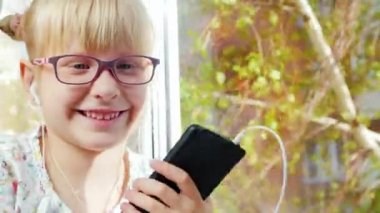 Komik kız güler, kameraya benziyor. O kulaklıklar müzik dinler, bir akıllı telefon elinde tutuyor. Pencerenin arka plan üzerinde oturur