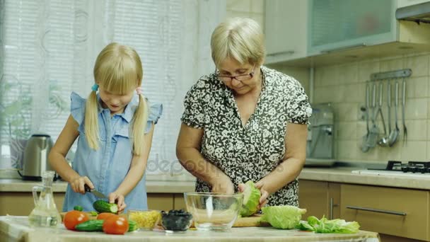Oma en haar kleindochter bereiden een salade in de keuken. Hebben een goede tijd, lachen, het meisje helpt oma — Stockvideo
