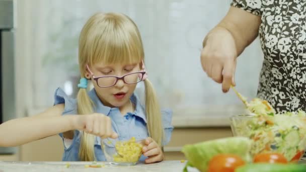 Uma garota engraçada come uma salada de uma tigela grande, ao lado de sua avó faz uma salada. Uma visita à minha querida avó, uma tradição de alimentação saudável — Vídeo de Stock