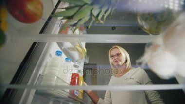 Işık gece snack, sağlıksız yiyecek. Gözlüklü genç bir kadın bir buzdolabı açar, içecekler suyu ve elma alır. Buzdolabı içinde görüntülemek