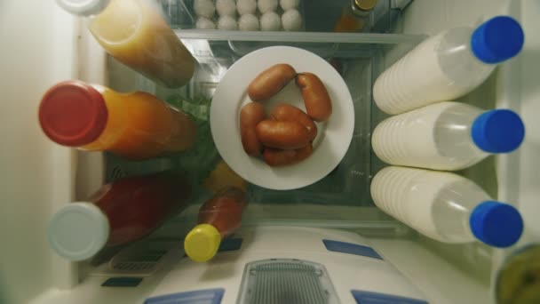 Snack nocturno y comidas no saludables y no regulares. Una mano de hombre toma una salchicha y una botella de jugo de la nevera, una vista desde el interior — Vídeos de Stock