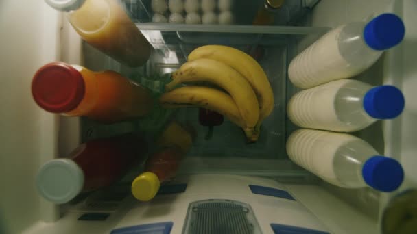 El niño saca un plátano del refrigerador. Snack de frutas fácil. Una vista desde el interior del refrigerador. Vista de ángulo alto — Vídeos de Stock