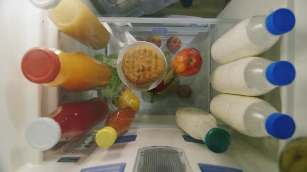 Выбор между здоровой и нездоровой пищей. Сначала рука в холодильнике забирает яблоко, а потом жирный бургер. Вид изнутри холодильника — стоковое видео
