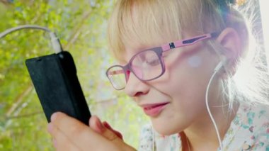 Pembe gözlüklü olumlu bir neşeli kız portresi. O pencereden güneşin telefon kullanır. Bahar ruh hali