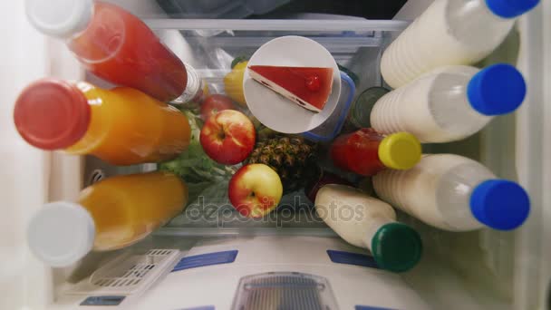 Un bocadillo rápido. Una mujer toma un pastel del refrigerador y muerde una manzana. Vista desde el interior del refrigerador — Vídeos de Stock