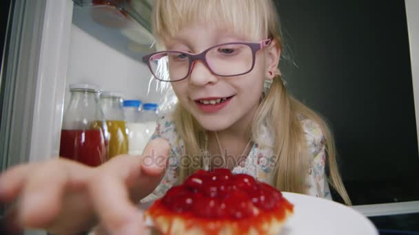 Egy kislány titokban íze egy eper torta belsejében a hűtőben. Gyermekkori csínyek, boldog gyermekkor — Stock videók