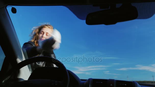 Joven mujer atractiva limpiando el parabrisas de un coche. Vista desde el interior del coche. Sobre el fondo de un cielo azul rojo en un día claro — Vídeos de Stock