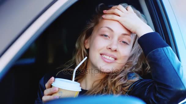 Portret młodej kobiety niezależne w samochodzie. Siada za kierownicą, patrzy w kamerę, trzyma kieliszek kawy w ręku uśmiechy. — Wideo stockowe