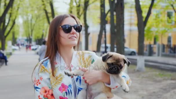 Ходити з цуценя в місті. Молода жінка з собакою на її руках, ходити в міському парку. Стедікам постріл — стокове відео