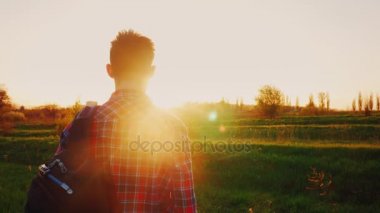 Bir genç bir sırt çantası ile ileri güneş ve ufuk için görünüyor. Arkadan Görünüm. Kavram - umut, yeni ufuklar, macera