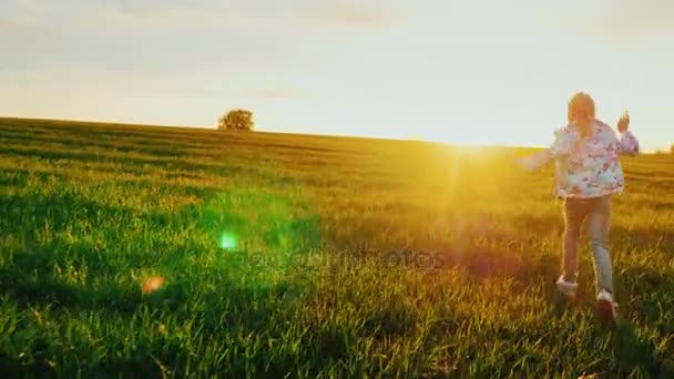 Una ragazzina corre sul campo come un aeroplano. Verso il tramonto. Concetto - energia di gioventù, infanzia felice, sogni. Steadicam shot — Video Stock