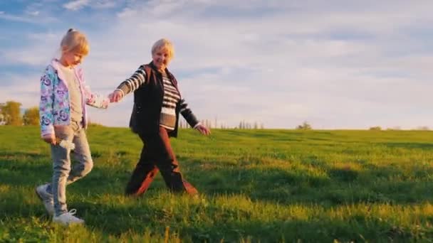 En senior kvinna promenader i dotterdottern. De går mot bakgrund av ett pittoreska landsbygdens landskap vid solnedgången — Stockvideo