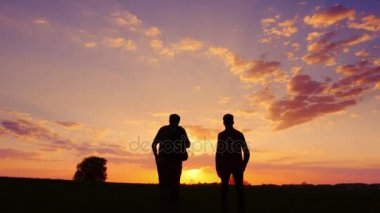 İki adamın - oğul ve baba siluetleri birlikte gitmek günbatımı karşılamak için. Arkadan Görünüm. Steadicam atış