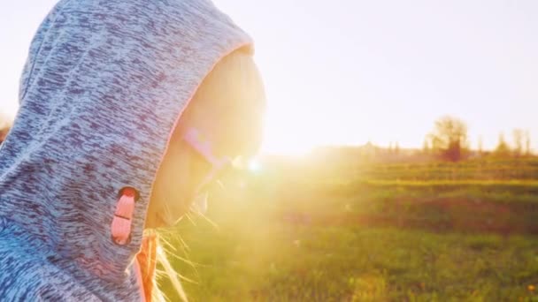 Portrait d'une petite fille en costume de sport. Il a une cagoule sur la tête. Debout dans le profil au coucher du soleil — Video