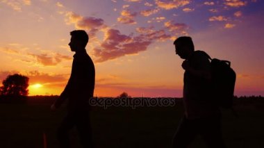 Baba ve oğul alan gün batımında yürüyor. Yan görünüm, babası bir sırt çantası taşıyor. Kavram - yeni başlangıçlar, umut, seyahat. Steadicam atış