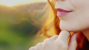 Gün batımı, yakın çekim-sadece dudaklar düşünceli bir kadın duruyor ve el çerçeve içinde görünür. Hafifçe gülümsüyor. Kadın güzelliğinin