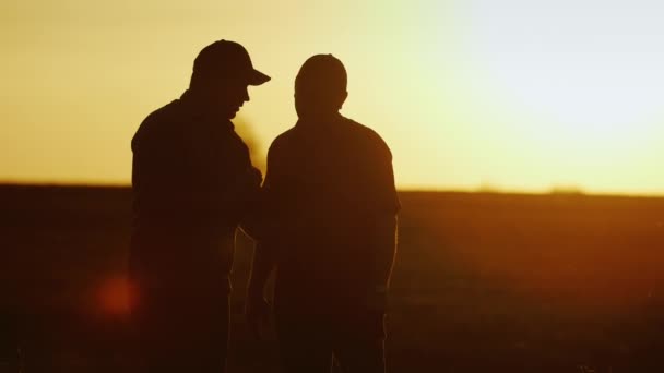 解决农业综合企业。两个男性农民沟通在球场上，使用一台平板电脑-握手。在日落时的剪影 — 图库视频影像