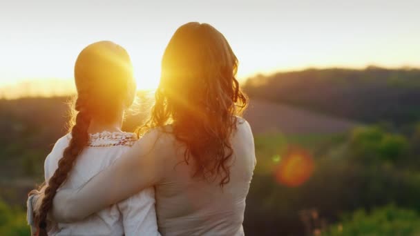 Mamãe gentilmente beija seu templo filhas. Juntos admiram o belo pôr-do-sol. Visão traseira — Vídeo de Stock