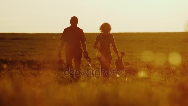 Agricultores - um homem e uma mulher caminhando pelo campo ao pôr-do-sol. Leve uma planta cultivada de sementes de árvore, uma lata de rega e uma pá. Conceito - trabalho no jardim, voluntariado, uma nova vida — Vídeo de Stock