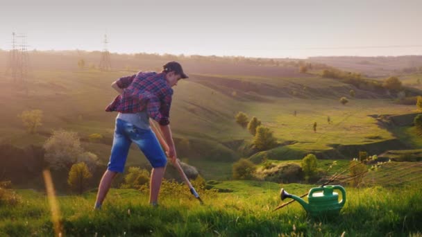 Un jeune homme de 17 ans plante un arbre. Creuser un trou avec une pelle, à côté d'un semis de pommier. Dans le contexte d'un beau paysage. Travail des bénévoles, protection de l'environnement — Video