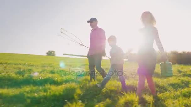 Eine Bauernfamilie mit einem kleinen Sohn geht zusammen, um einen Baum zu pflanzen. tragen die Apfelbaum-Setzlinge, Schaufel und Gießkissen. Steadicam-Aufnahme, Seitenansicht — Stockvideo