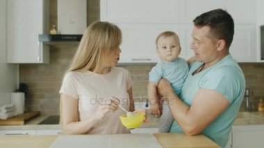 Genç bir anne 10 aylık oğlu yemeye hazırlar. Babası onun yanında duruyor ve çocuk onun kollarında tutar. Bebek maması, bebek ile mutlu aile