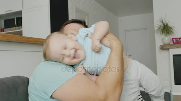 Una familia joven y feliz está jugando con un hijo de 10 meses en casa. Papá sostiene a un bebé en sus brazos, mamá está sentada a su lado, sonriendo — Vídeos de Stock