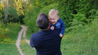 Genç sağlıklı baba ile oğlu parkta yürüyor. Bebek onun kollarında, dikiz taşır