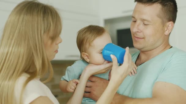 The kid drinks water from the cup. His parents are holding — Stock Video