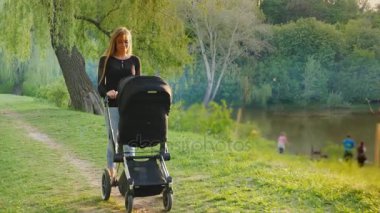 Bir bebek arabası ile parkta yürüyen genç beyaz anne. Steadicam atış