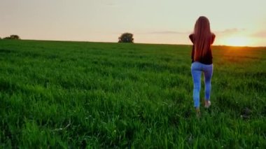 Genç bir kadın güzel bir yeşil çayır gün batımında yürüyor. Arkadan Görünüm