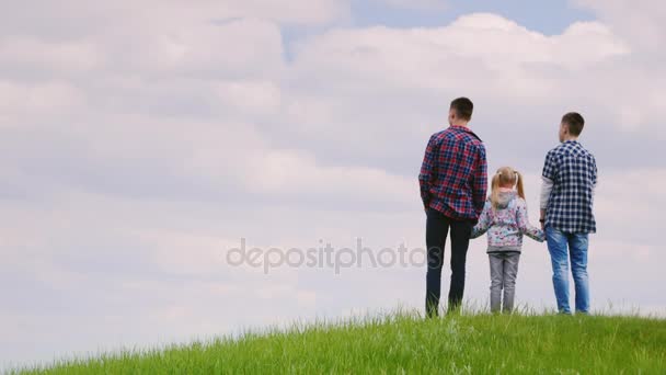 Группа детей - двое подростков и девочка 6 лет, стоящая на холме, глядя на горизонт. Вид сзади — стоковое видео