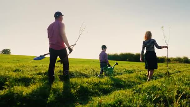 Задний план: Семья фермеров с маленьким сыном собираются посадить дерево. Инструменты для сада и саженцы яблонь — стоковое видео