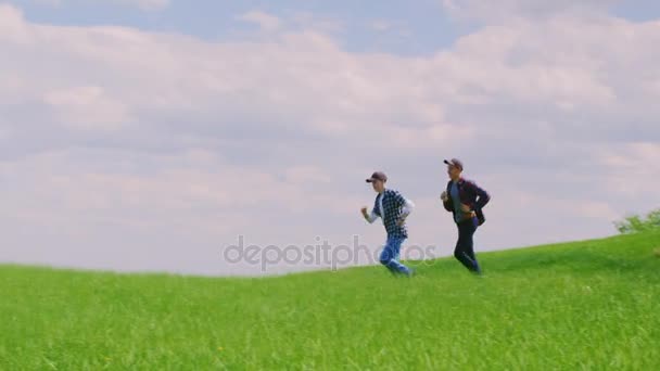 Два подростка бегут по зеленому холму — стоковое видео