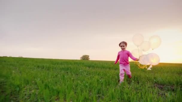 Rolig tjej 4 år körs på en grön äng med ballonger — Stockvideo