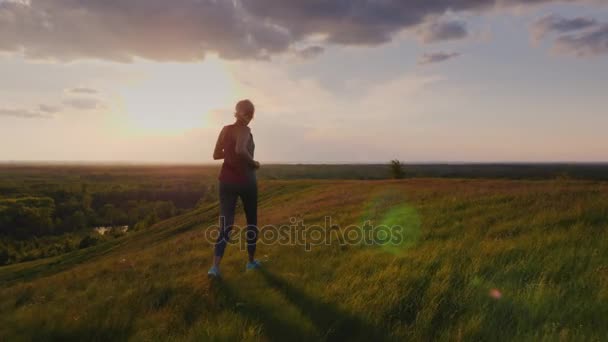 Mladá žena běhání v malebném místě při západu slunce. Pohled zezadu. 4 k video zpomaleně — Stock video