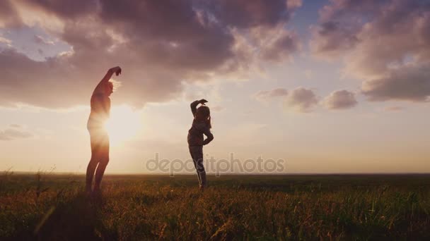 Jonge vrouw met haar dochter doen oefeningen bij zonsondergang. Ze staan in een pittoreske plaats. Gezonde familie. Slowmotion 4 k video — Stockvideo