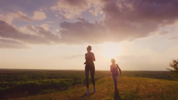 Mamá e hija corren en un lugar pintoresco al atardecer. Estilo de vida activo y familia sana. 4K video en cámara lenta — Vídeos de Stock