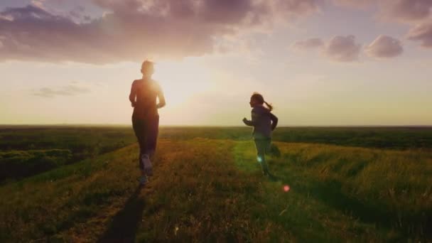 Visão traseira: Mãe e filha correm em um lugar pitoresco ao pôr do sol. Estilo de vida ativo e família saudável. Vídeo em câmera lenta 4K — Vídeo de Stock