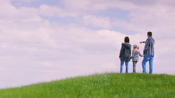 En familj på tre personer - far, mor och dotter 6 år gammal, står på en grön kulle. Ser fram emot horisonten, bakifrån. Copyspace copmosition — Stockvideo