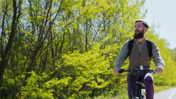一个年轻时髦人留着胡子在自行车道上骑自行车。喜欢旅行的春天森林在好天气背景。健康的生活方式 — 图库视频影像